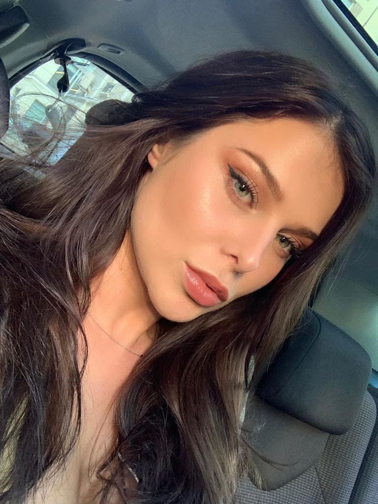 A close-up selfie shows a woman with long dark hair and a necklace leaning against a car seat near a window.
